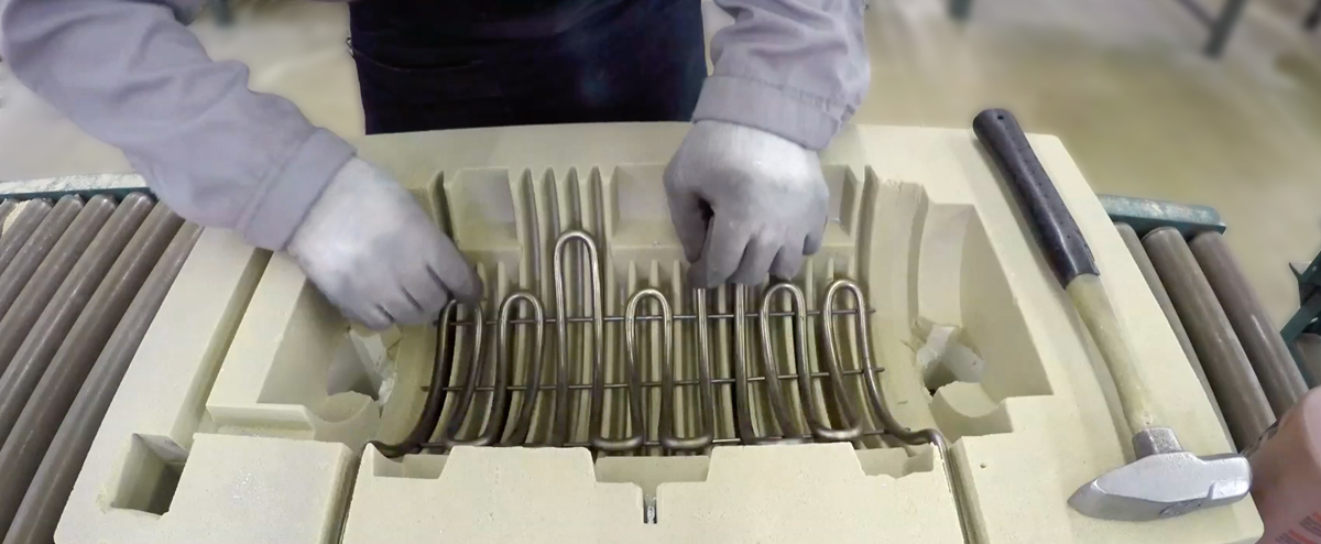 Skilled worker placing tubular heating element into sand mold for casting