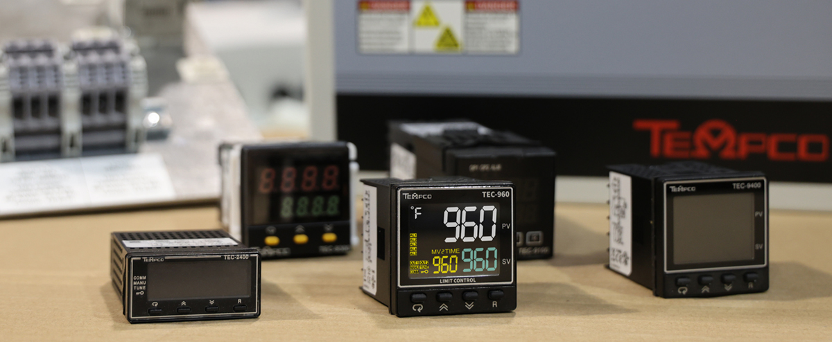 temperature controllers on a table in front of the face of a control panel and parts